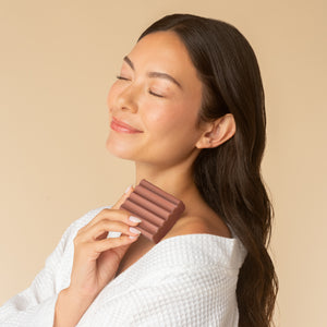 Woman holding Kitsch Amber Shores Body Wash Bar near her chin with eyes closed enjoying the woody aquatic fragrance