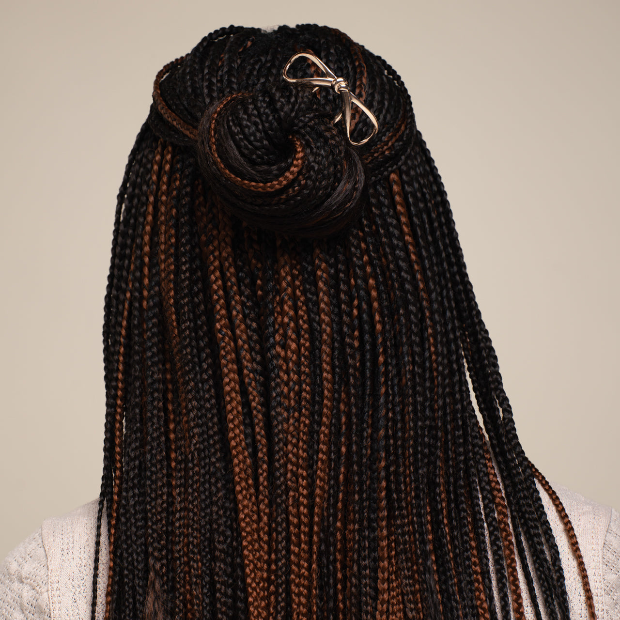 Woman with styled hair bun wearing a white sweater against a beige background
