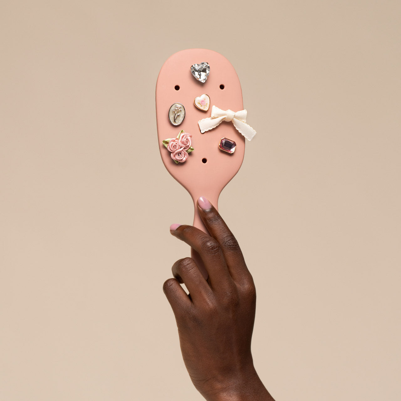Pink hairbrush with decorative pins held by a hand against a beige background