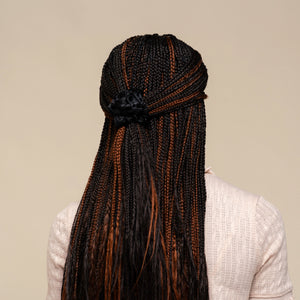 Person with micro braided hair wearing the kitsch black rosette ruched scrunchie against a neutral background
