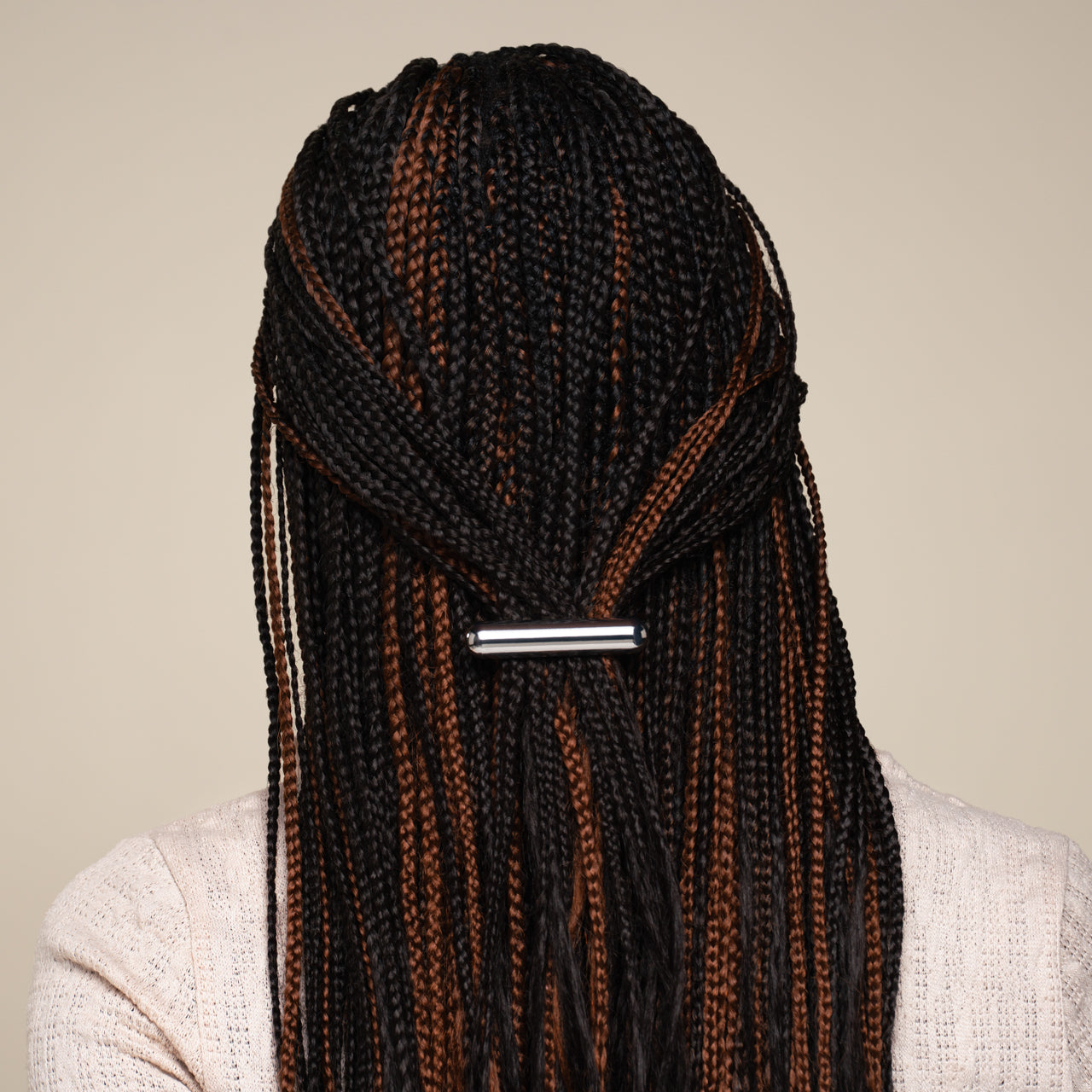 Person with micro braids featuring black and brown colors secured with a kitsch silver hair clip on a beige background