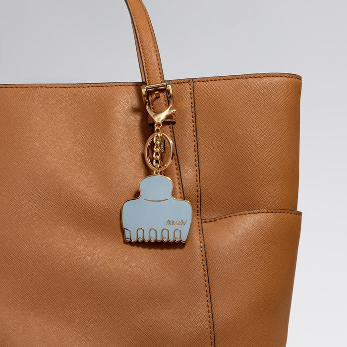 Brown leather handbag with Metal enamel keychain of the kitsch Haze Blue Cloud Clip  on a light gray background