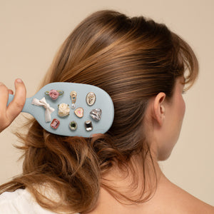 Person using a decorative hairbrush with various embellishments in their hair.