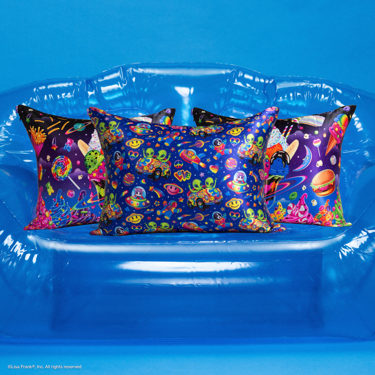 KITSCH Lisa Frank x Kitsch Satin Pillowcase in Zoomer & Zorbit and Lisa Frank x Kitsch Satin Pillowcase in Saturn Sundae — three satin pillowcases on a clear blue inflatable couch, Zoomer & Zorbit print in front with Saturn Sundae behind — tame frizz and reduce breakage, prevent facial creases — mix and match Lisa Frank prints for smoother hair and skin overnight