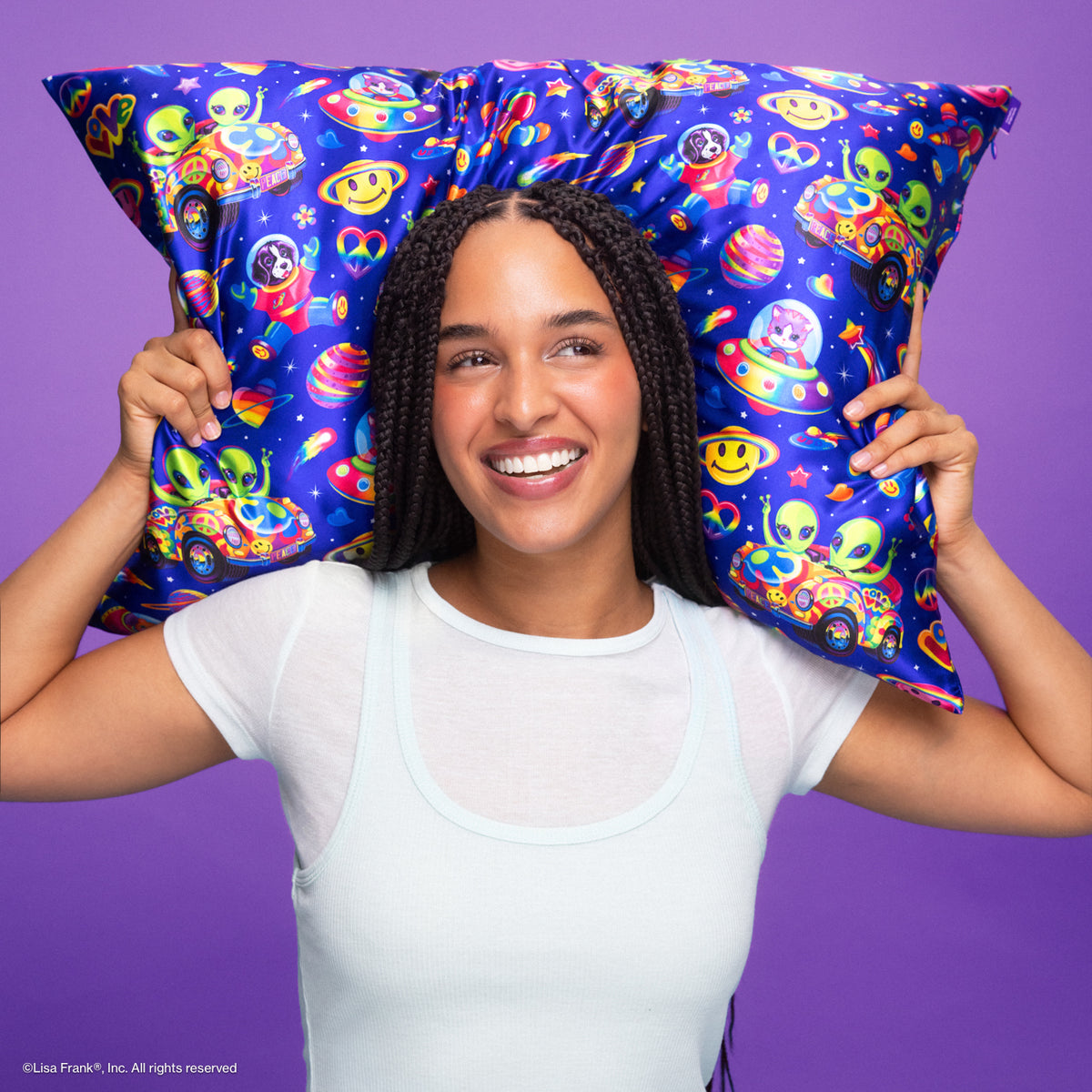 KITSCH Lisa Frank x Kitsch Satin Pillowcase in Zoomer & Zorbit — smiling model with long braids holding the blue alien space-print satin pillowcase behind her head — gentle on skin, hair, lashes, and brows, stays cool all night — sleep on satin to wake up with smoother hair and skin